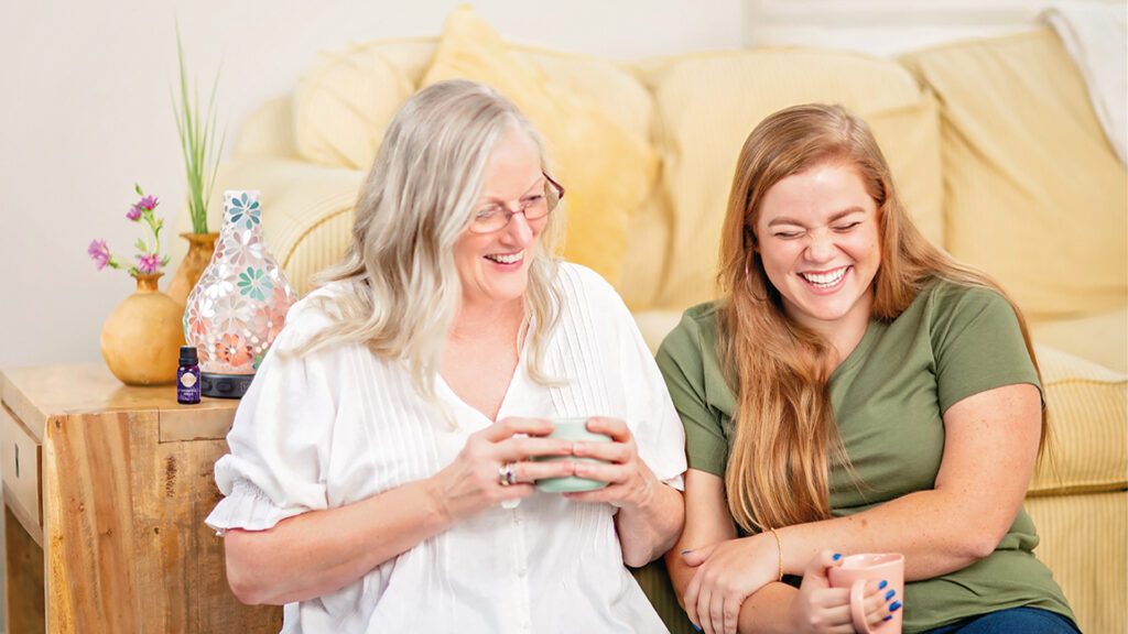 Two woman laughing and enjoying each other's company while drinking from mugs.