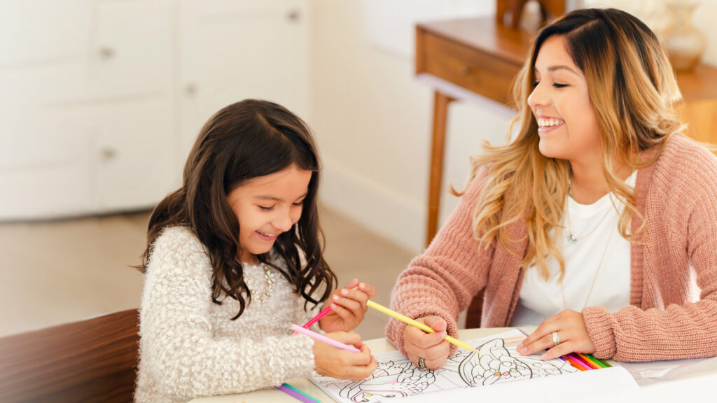 A woman and a young girl smiling while coloring in a coloring book together.