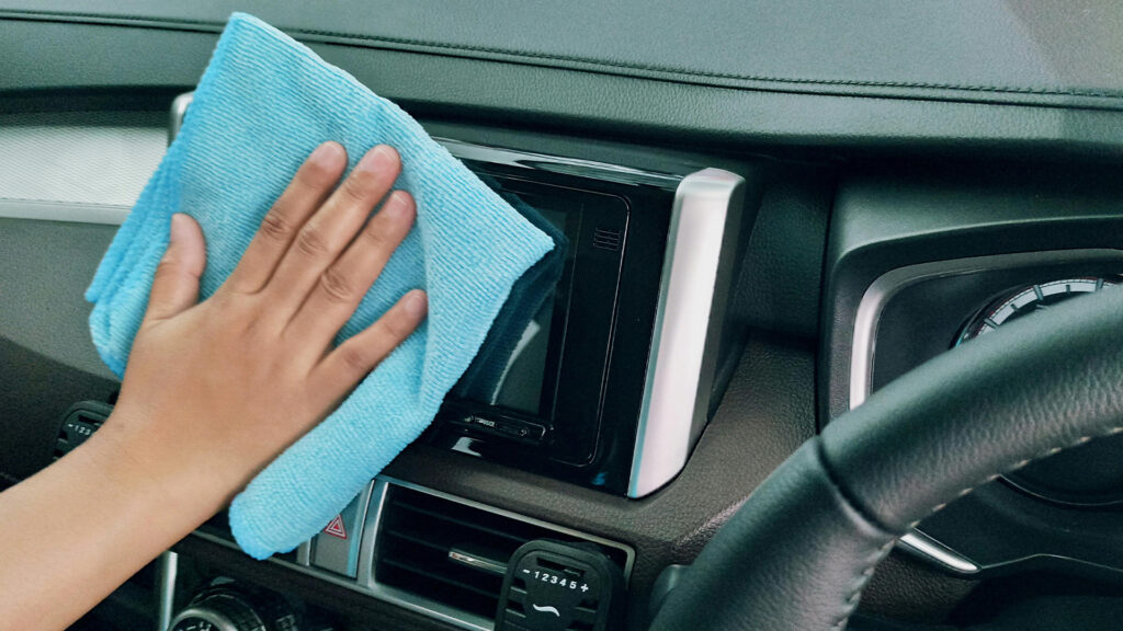 A hand holding a blue microfiber towel wiping clean a car's center console.