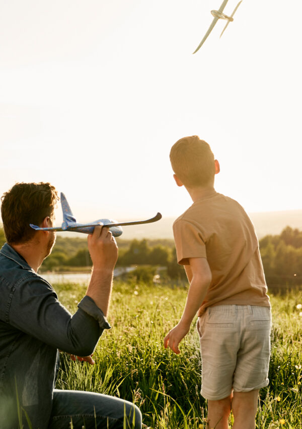 A father and son playing with toy airplanes in a field.