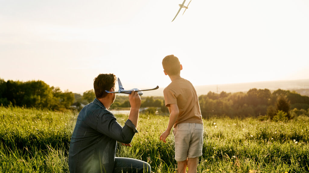 A father and sun fly model airplanes together in a field.