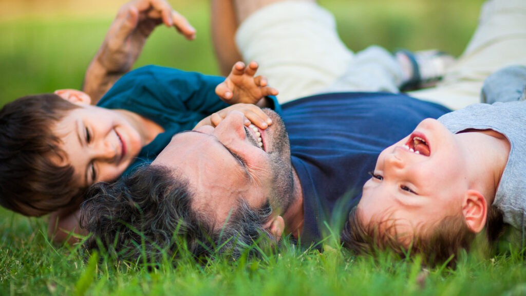 A father and his two children laugh together while lying in the grass.