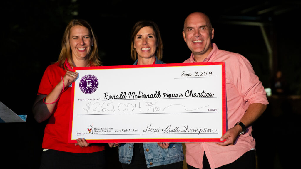 Heidi and Orville Thompson, and one other person, hold a check for $265,004 made out to the Ronald McDonald House Charity.