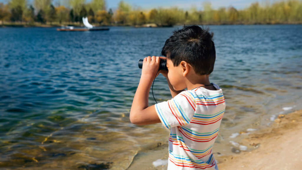 A child uses binoculars to look across a like.