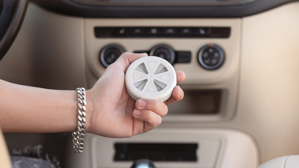 A Scentsy travel twist held near the center console of a car.