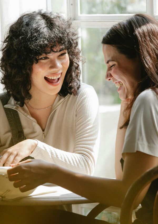 A mother and daughter laughing together at a table.