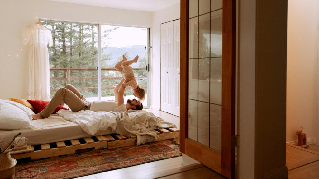 A father lays on a bed and tosses his child into the air.