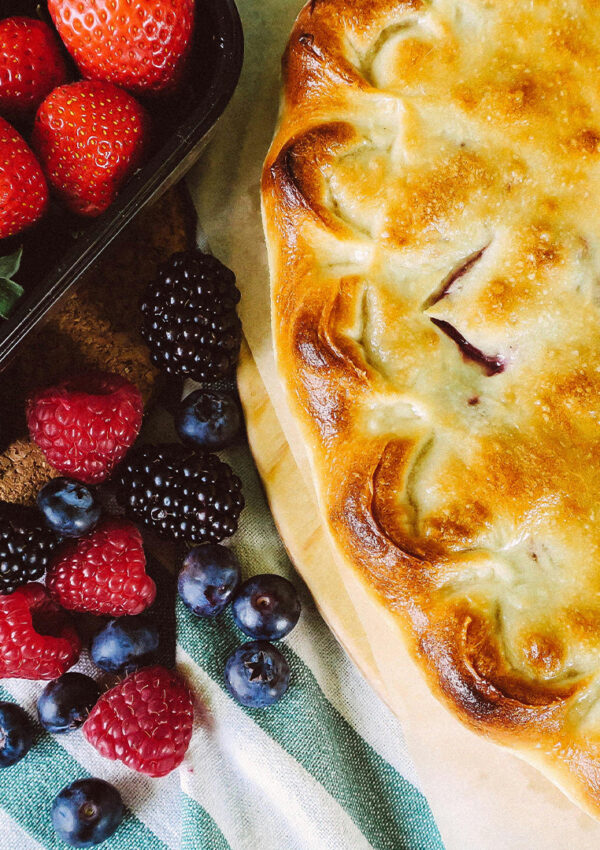 Berry pie sitting on a table with fresh berries beside it.