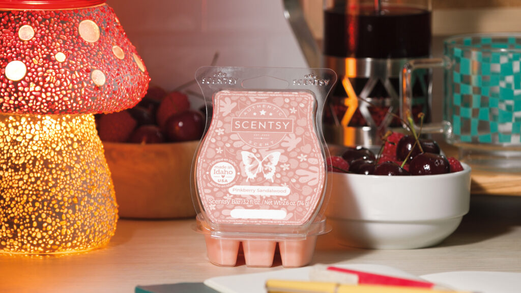 A Pinkberry Sandalwood Scentsy Wax Bar sits on a desk beside a Scentsy warmer and a bowl of fresh fruit.