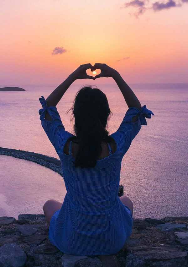 Person sitting on a rocky outcropping watching the sunset over the ocean below.