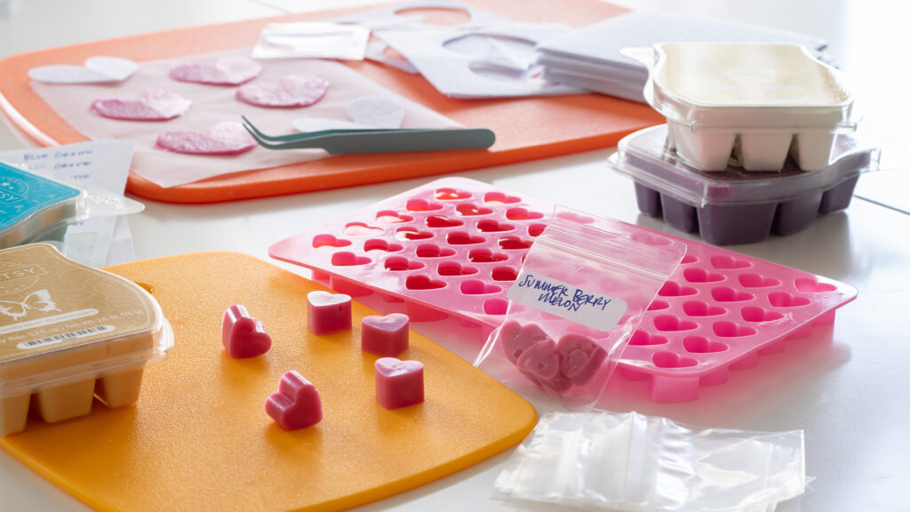 Scentsy wax cubes in the shape of little hearts all gathered on a tabletop amidst crafting supplies.