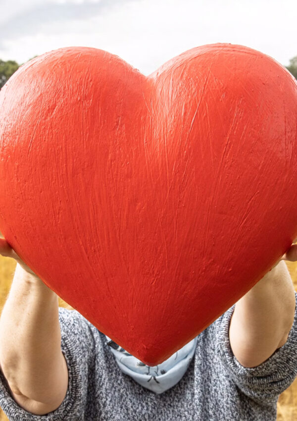 A person holding a large decorative heart in a rural grain field.