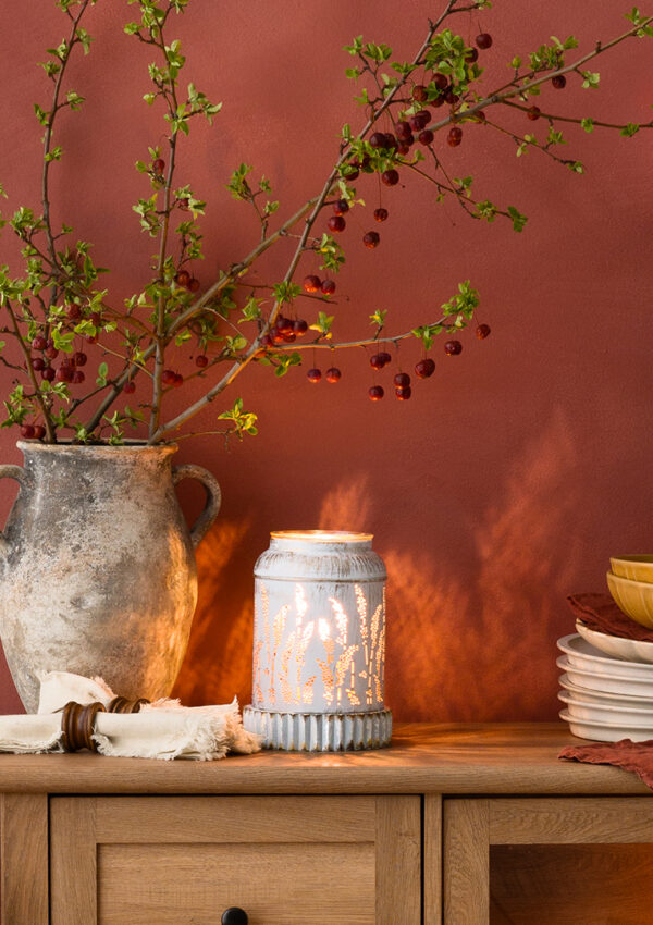 A kitchen cabinet with a Scentsy warmer and Scentsy fragrance flower amidst plates, serving dishes, and other home decor.