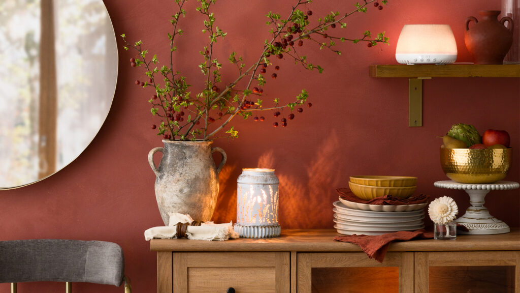 A kitchen cabinet with a Scentsy warmer and Scentsy fragrance flower amidst plates, serving dishes, and other home decor.