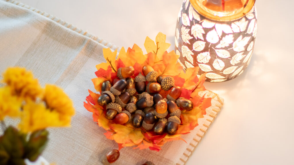 A DIY snack dish full of acorns sits beside a Scentsy warmer on a table decorated for autumn.