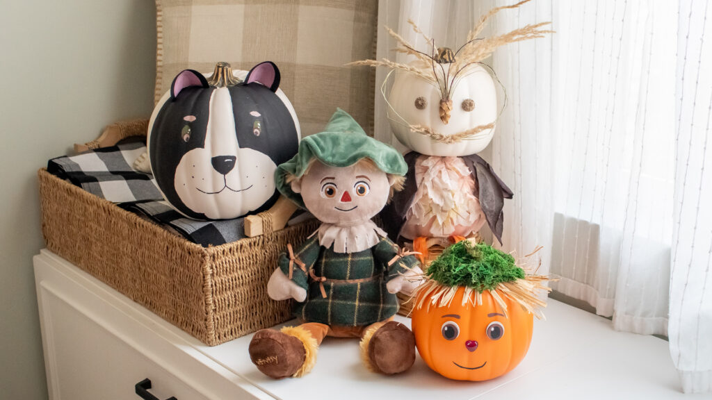 Scentsy's Scarecrow buddy is propped up next to several pumpkins that have been artuflly painted decorated with halloween and harvest themes.