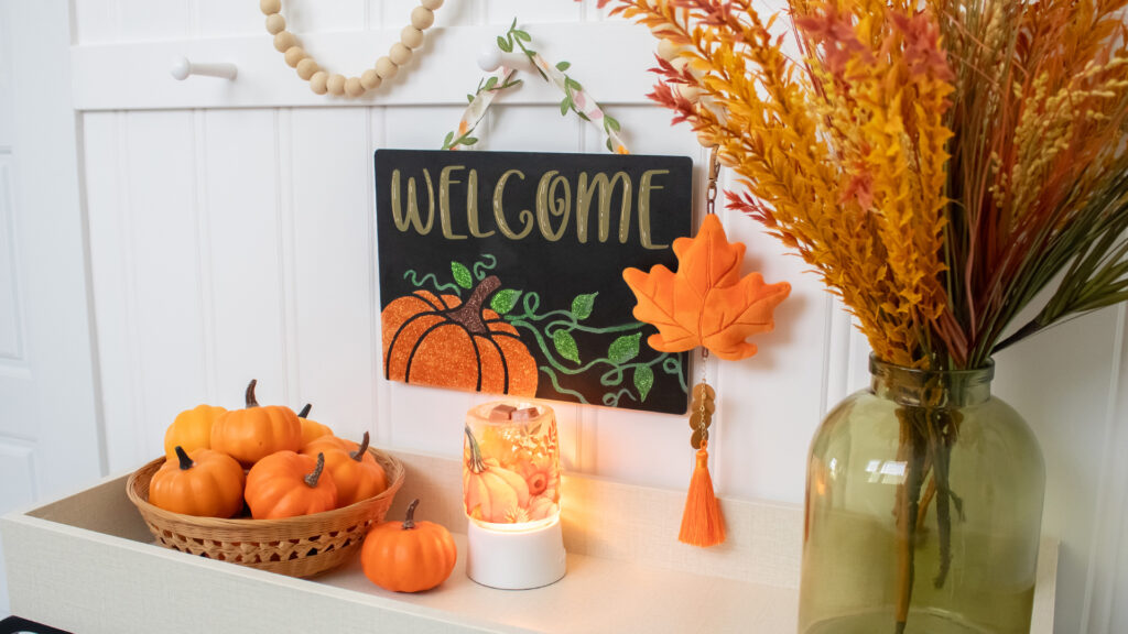 A welcome sign with a painted pumpkin sign sits above a pumpkin themed display table.