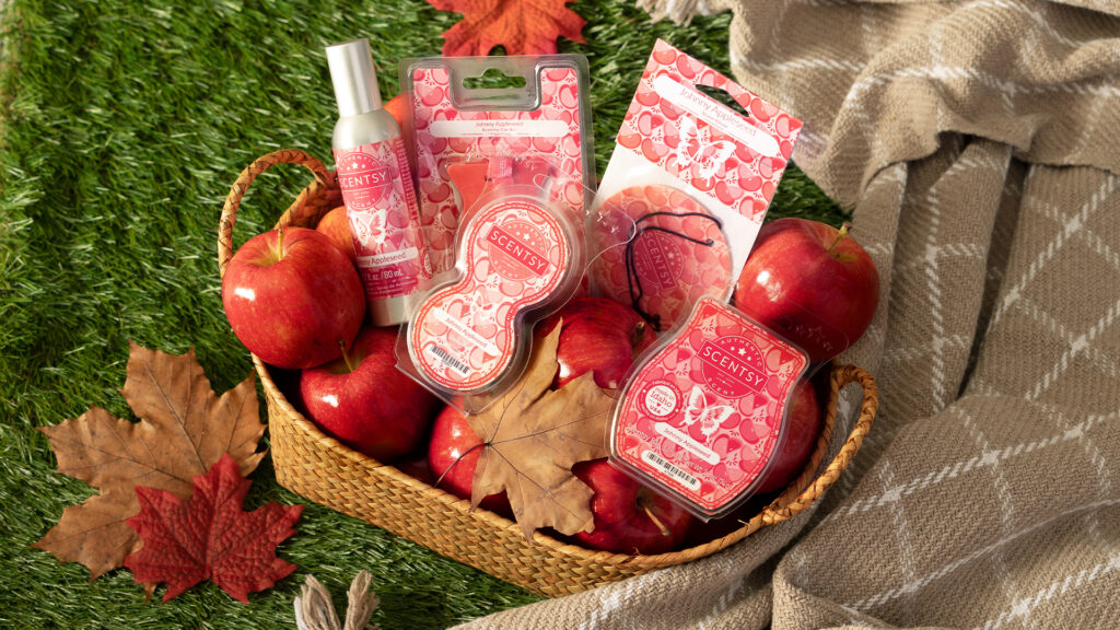 A basket packed with Scentsy Johnny Apple Seed fragrance products, fresh apples, and fall leaves.