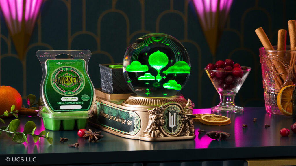 A stylized set with fruit and spices indicating fragrance notes and the Wicked Scentsy Warmer and Wicked Emerald City Scentsy Bar.