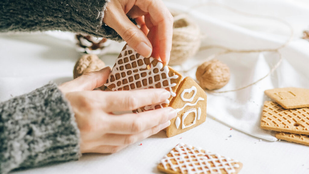 a pair of hands carefully building a gingerbread house.