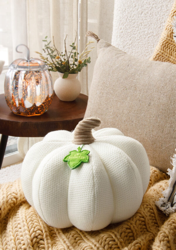 A cozy image of the Lumina Pumpkin Darling Decor pillow sitting on a soft couch with fuzzy blankets and soft cushions.