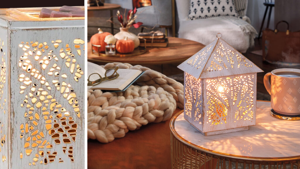 The Scentsy Forest Light Warmer shown placed on a wicker side-table and styled with white, beige decorations that give the feeling of fall and neutral tones.