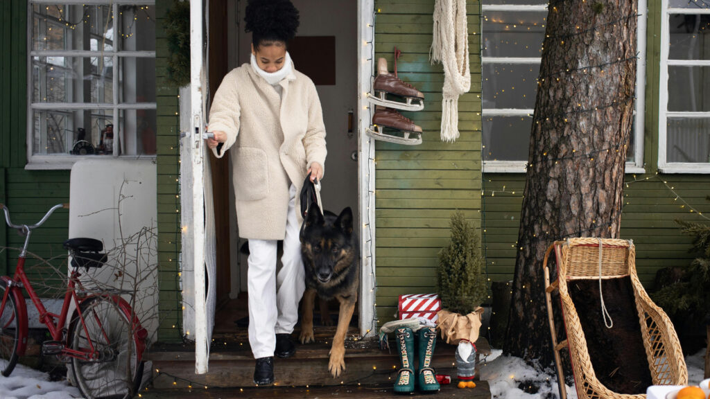 A woman, bundled in a coat and scarf, and her German shepherd step from her front door into the wintery air.