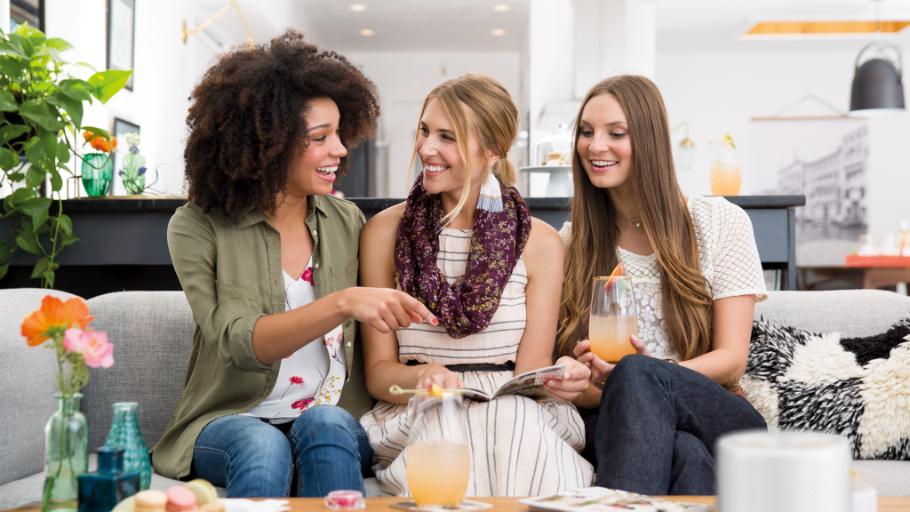 Three woman sit on a couch at a Scentsy Party together.