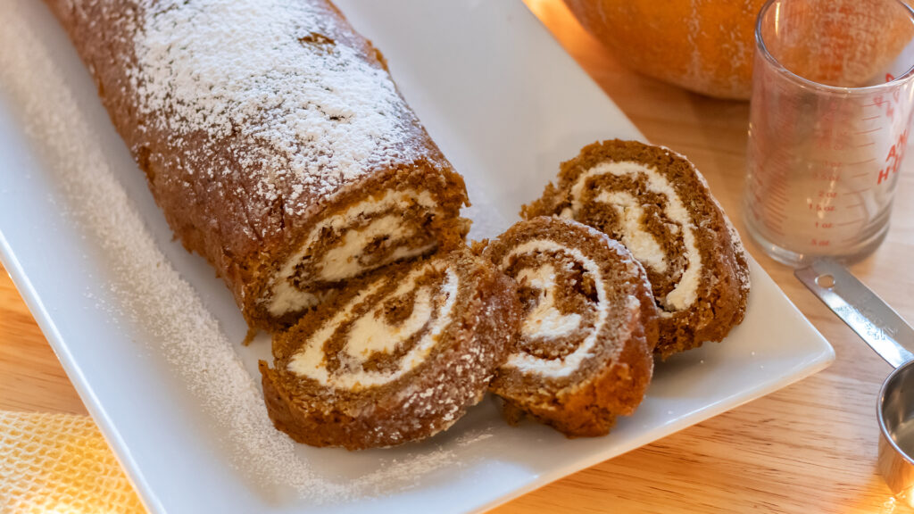 A photo of a pumpkin Swiss roll, with several slices cut to show the creamy swrirl of filling on the inside.