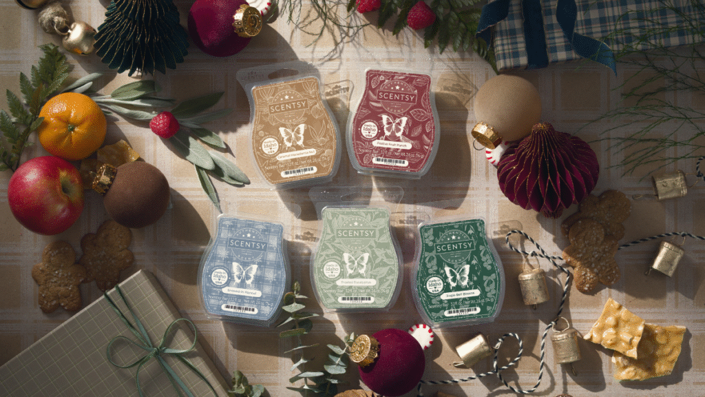 Scentsy Wax Melt Bars from the Holiday Collection sit on a table surrounded by Christmas ornaments, fruits, herbs, and sweat treats.