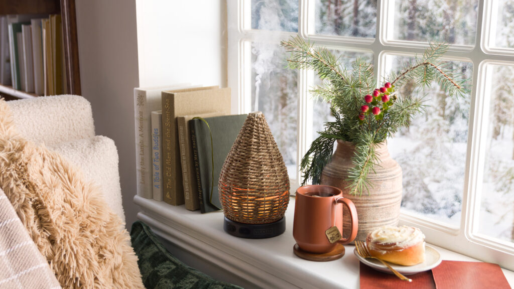 A cozy book nook featuring a Scentsy diffuser, a comfy chair, books, a cinnamon roll, and tea.