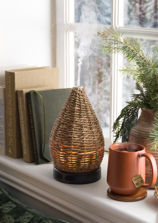 A cozy book nook featuring a Scentsy diffuser, a comfy chair, books, a cinnamon roll, and tea.