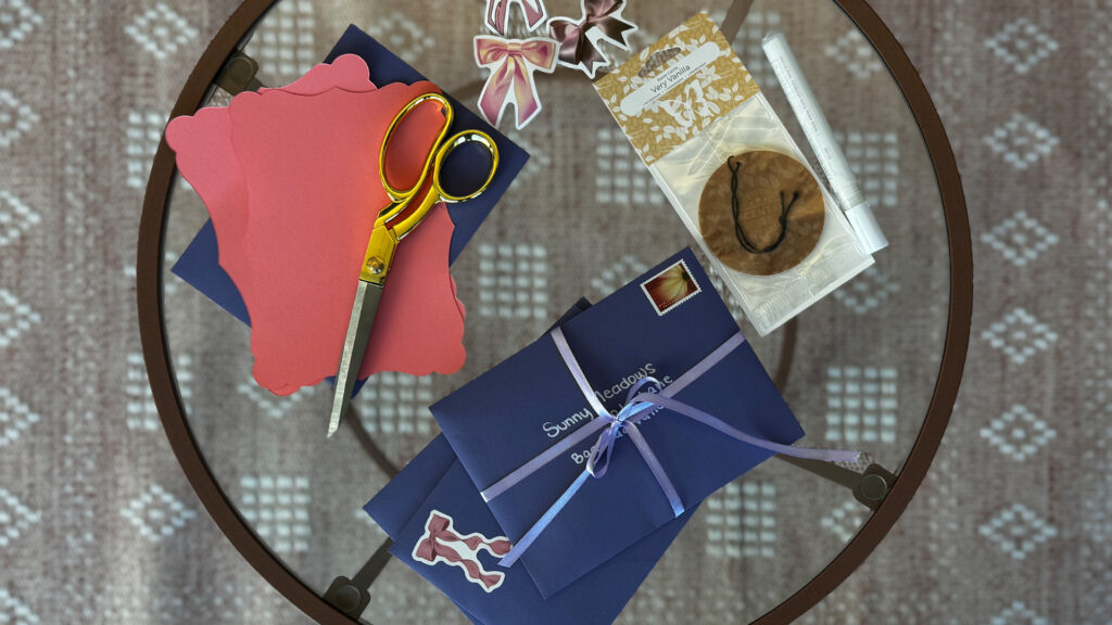 Letters, craft paper, stickers scissors, and Scentsy Scent Circles sit on a table.