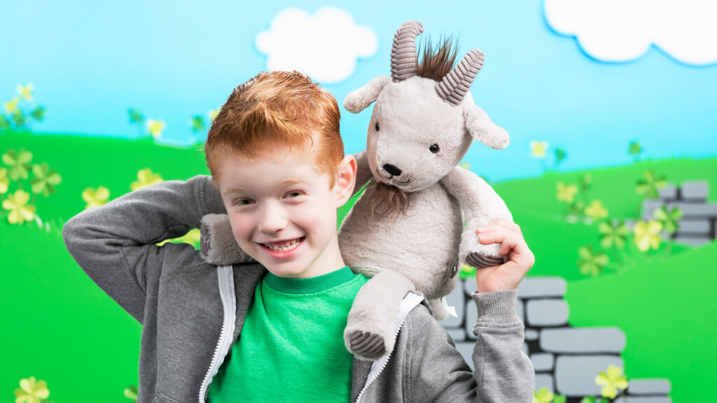 A young boy, smiling and holding Glendon the Goat Scentsy Buddy on his shoulders. 