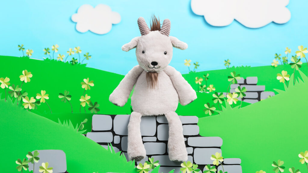 Glendon the Goat Scentsy Buddy sits in a cartoon prairie beneath blue, cloud-filled skies.