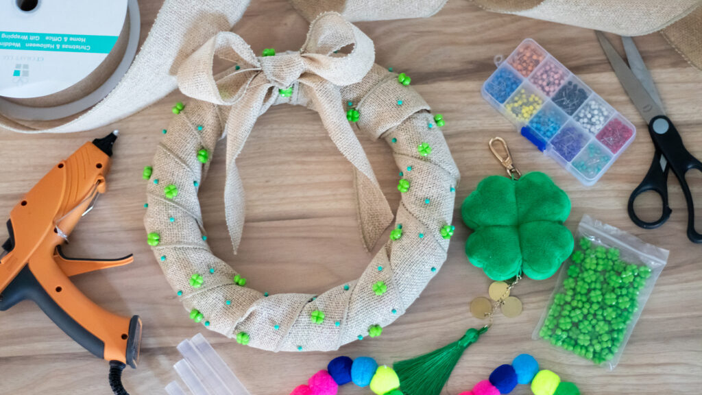 A half-finished half-finished St. Patrick's Day wreath made of cloth and decorated with clover charms sits among crafting supplies and beside the Scentsy Four Leaf Clover Charm Clip