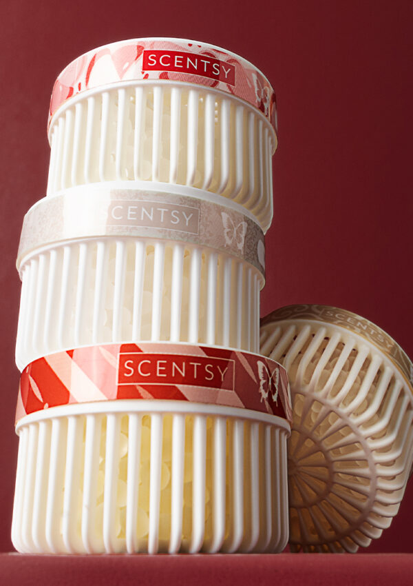 Four Scentsy Pods, with white plastic vents and red strip-lables along the top, sit stacked upon one another against a deep red background.