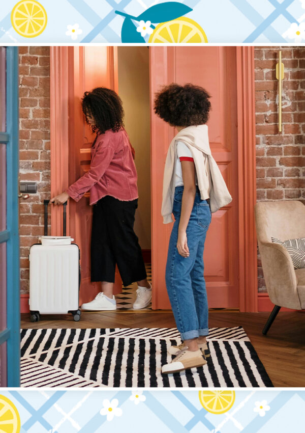 Two women with travel luggage stand in the entranceway of an vacation home.