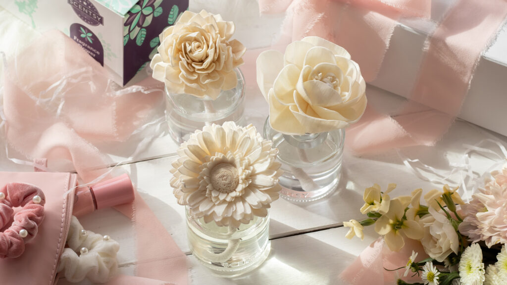 Three white Scentsy Fragrance Flowers sit together on a white wedding gift table adorned with flowers and pink ribbons and napkins.