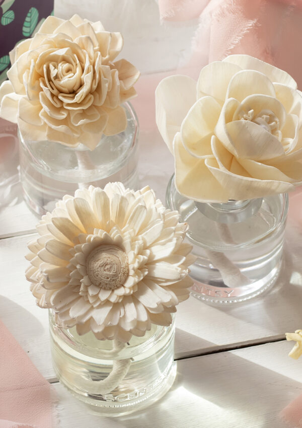 Three white Scentsy Fragrance Flowers sit together on a white wedding gift table adorned with flowers and pink ribbons and napkins.