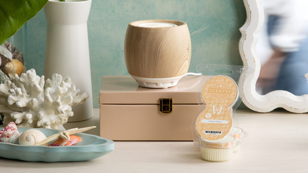 A Scentsy Air sits on a small tab box beside a Scentsy Pods Twin Pack and a small blue dish full of sea shells.