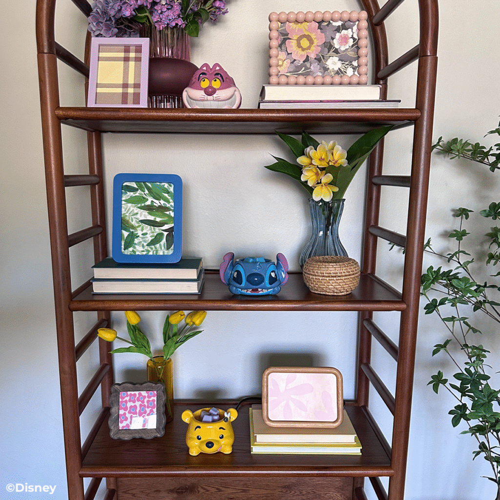 Pictures, frames, books, flower bouquets, and the Cheshire Cat, Winnie the Pooh, and Stitch Warm Fuzzies Wax Warmers are displayed on a decorative wooden shelf.