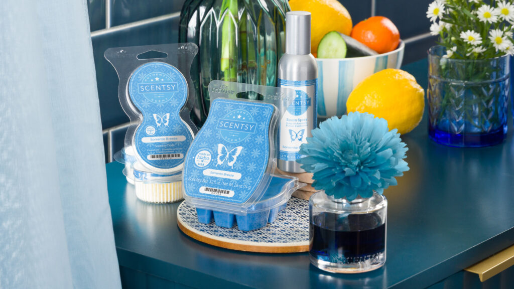 Scentsy Sorrento Breeze Pods, Wax Bar, Room Spray, Fragrance flower, and an assortment of citrus fruits all decorate a blue tabletop with matching bowls, cups, and plates.