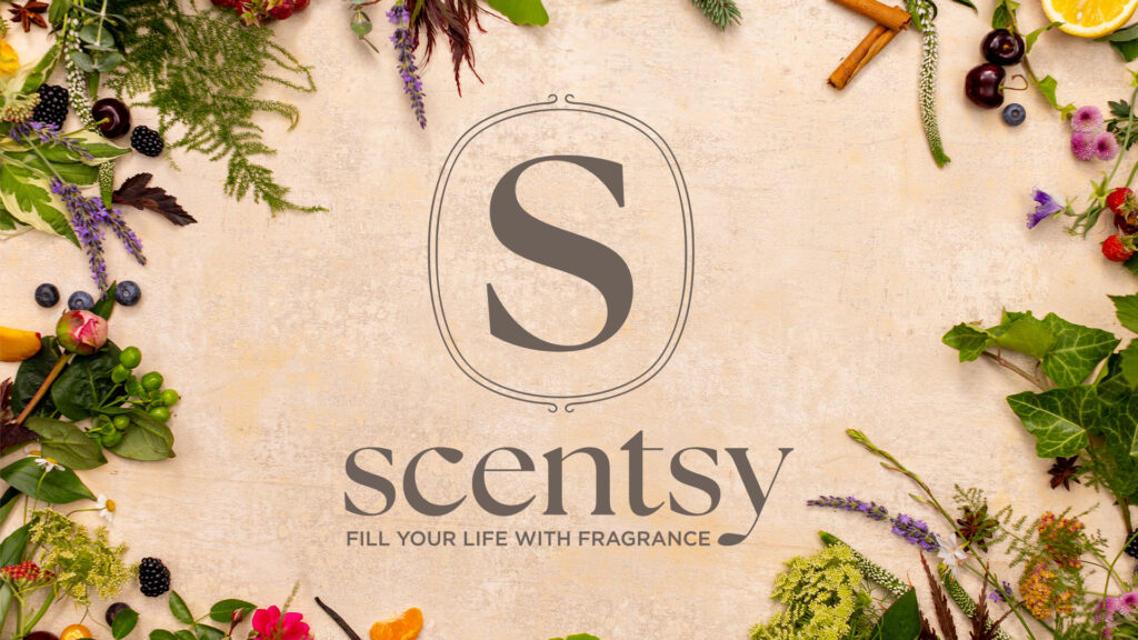 The new Scentsy Logo is depicted in a grassy yellow-green surrounded by a foliage border. The logo is an elegant S framed by a thin oval with the word Scentsy below.