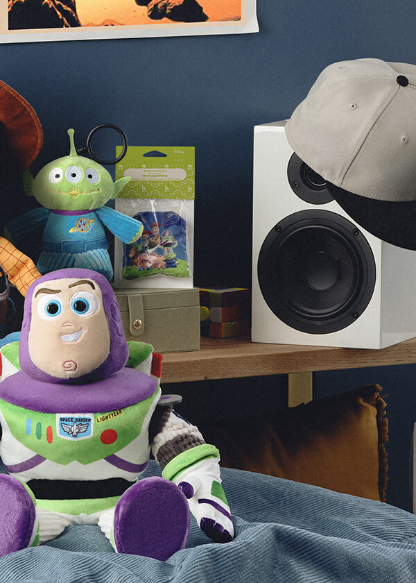 The Woody and Buzz Scentsy Toy Story Buddies are posed in a child's room decorated to look like Andy's Room with speakers, photos on the wall, and the Disney and Pixar Toy Story: The Claw - Scentsy Warmer.
