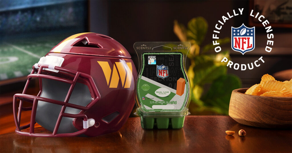 The Scentsy NFL Warriors Warmer sits on a table beside the Goal Line Scnetsy Wax Bar and a wooden bowl full of potato chips. A TV shows a football game in the background.