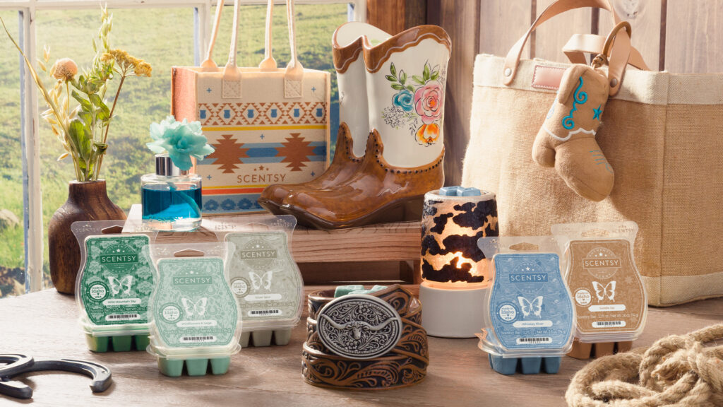 The Scentsy Wild Flowers and Wild Horses collection of wax bars and warmers is displayed in a farmhouse-style set in front of a window looking out over a pasture.