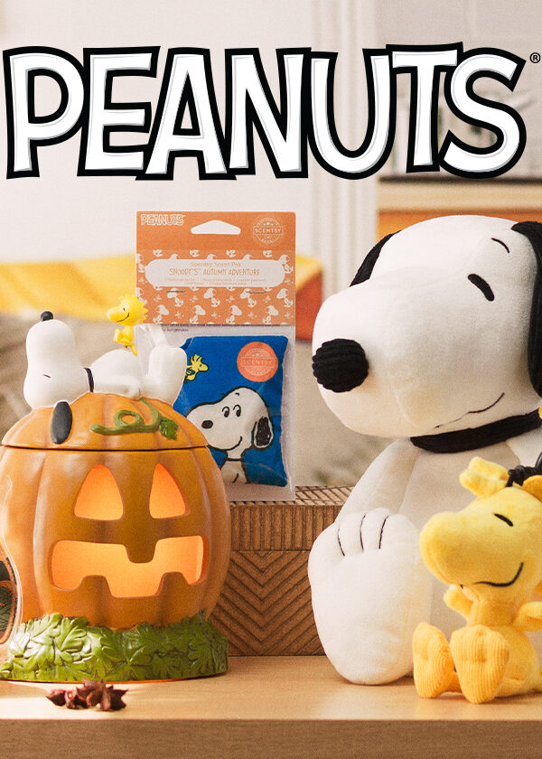 A Snoopy Scentsy Buddy stuffed toy sits beside a smaller Woodstock Buddy Clip stuffed toy on a wooden coffee table. Beside them are the Snoopy's Pumpkin Patch Scentsy Warmer, which depicts a large pumpkin with Snoopy sleeping on top, as well as the Snoopy's Autumn Adventure Wax Bar open beside the warmer. This Scentsy Peanuts collection sits in a warmly lit room with a yellow couch and paneled cabinets in the background.