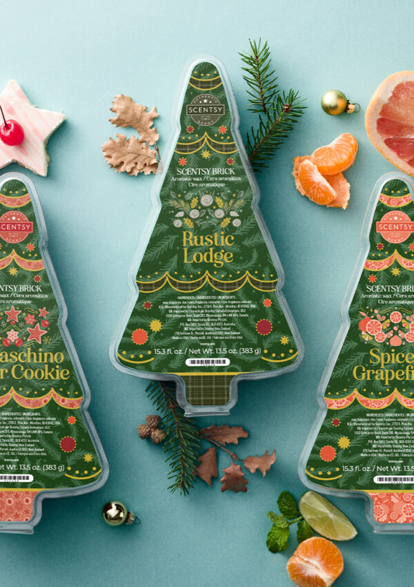 Four Christmas tree shaped Holiday Bricks from Scentsy with holiday scented wax melts sitting on a blue table surrounded cinnamon sticks, star-shaped cookies, pine needles, oranges, limes, walnuts, star anise, and ornaments - all of which represent fragrance notes and holiday cheer.