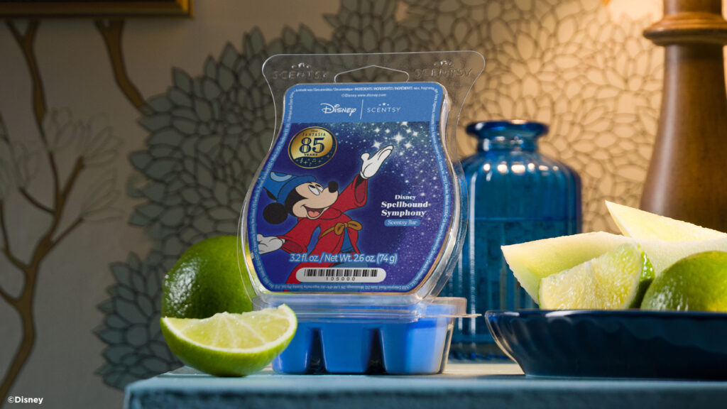 The Disney: Spellbound Symphony Scentsy Wax Bar sits on a tabletop. It's label depicts Mickey Mouse in his blue, magic hat from Fantasia's Sorcerer's Apprentice. The wax bar is surrounded by limes, and slices of slimes in blue bowls.